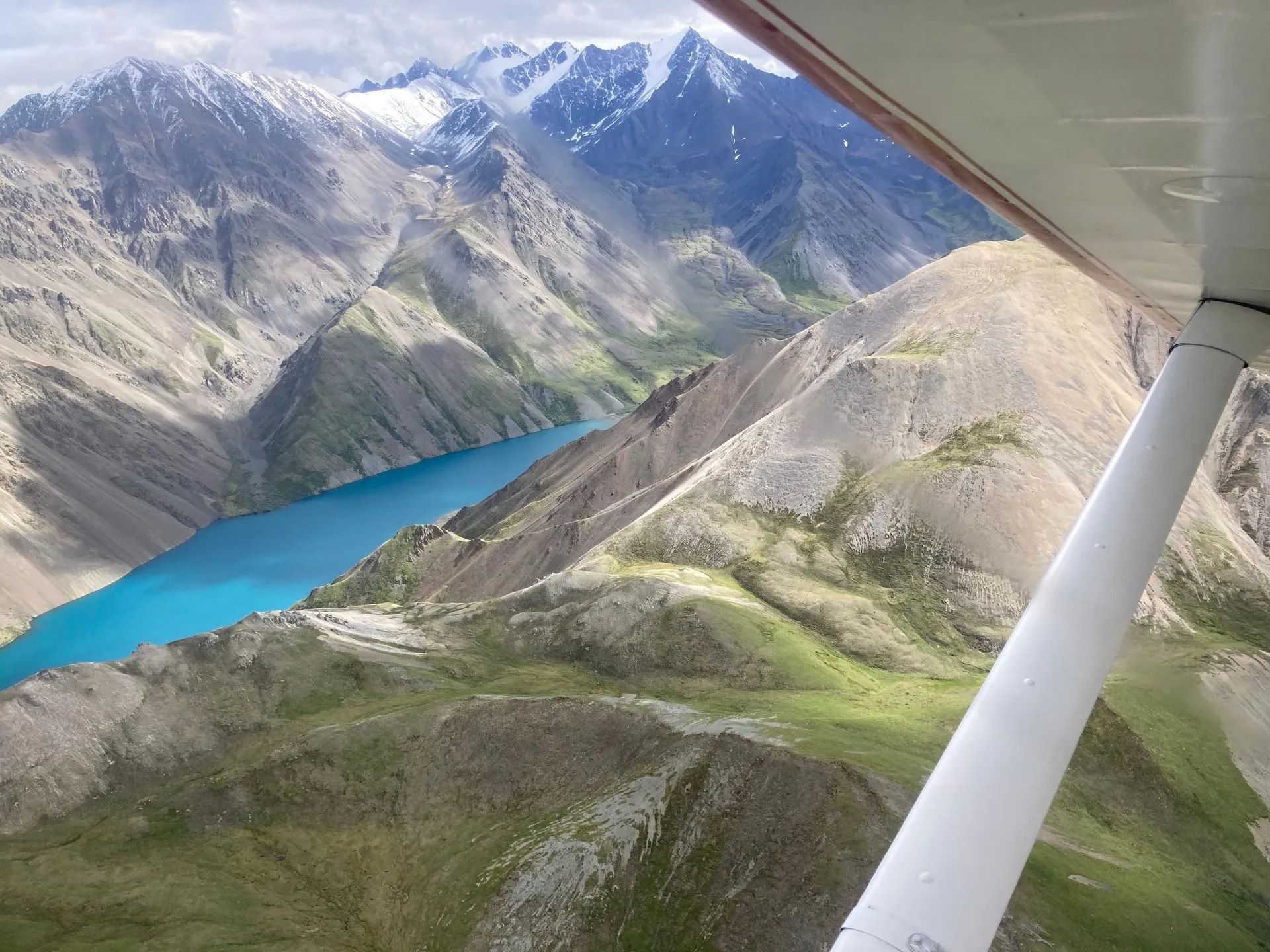 Aerial view of a bright blue lake surrounded by rocky mountains, seen from inside a small plane.