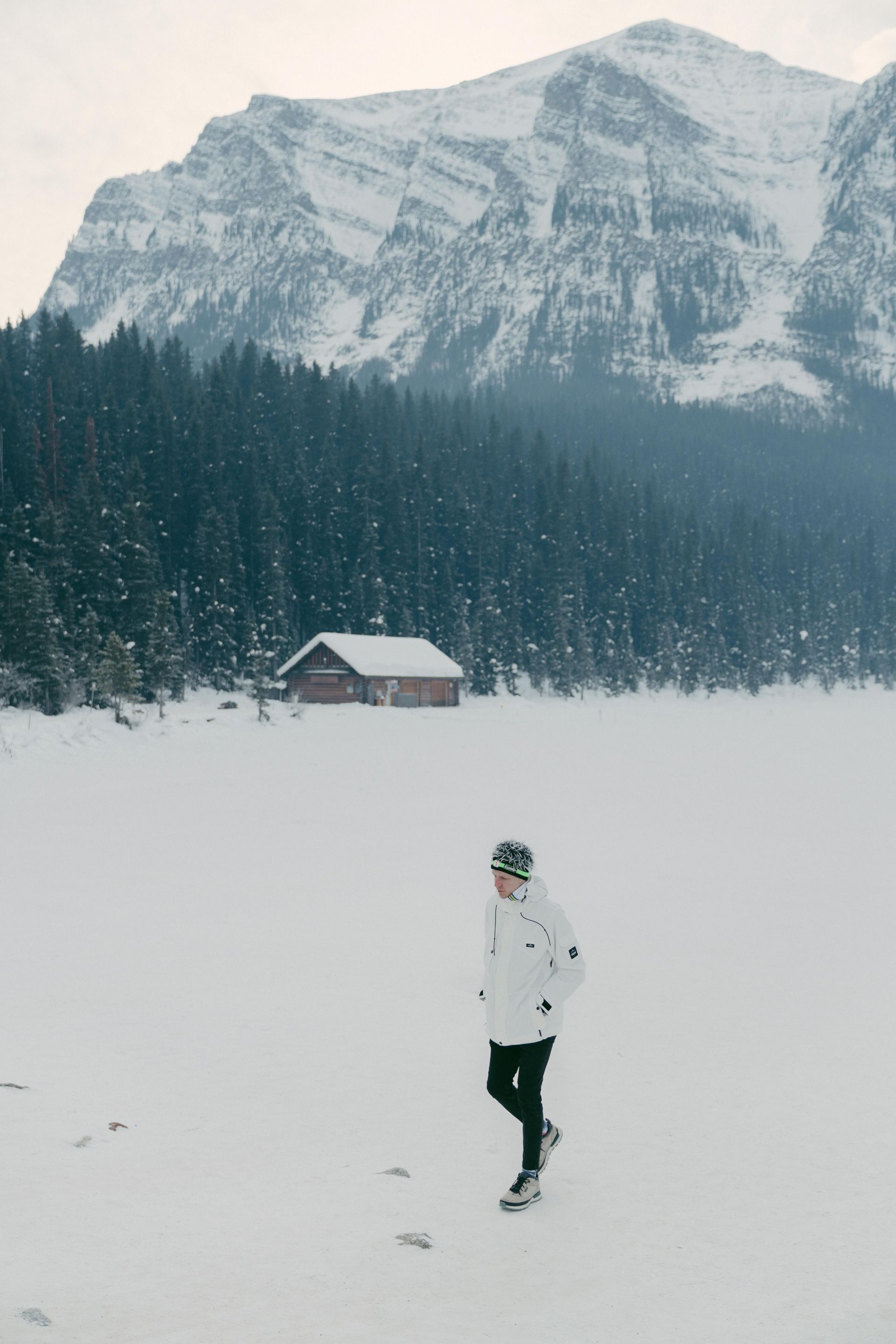 A person is walking through a snowy field in front of a mountain.