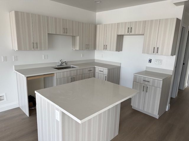 A modern kitchen with light gray cabinetry, white countertops, and a central island.