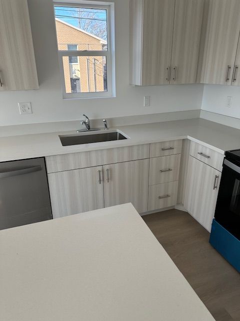 A modern kitchen with light cabinets and countertops, a stainless steel sink and dishwasher, and a window.
