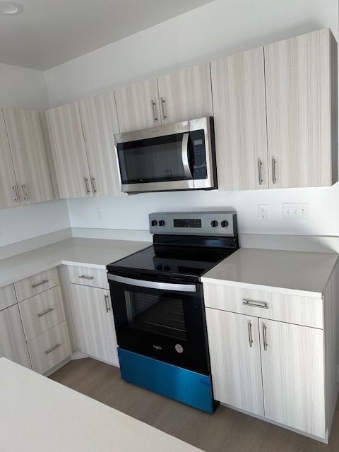 Kitchen with light wood grain cabinets, a stainless steel microwave and oven, and light countertops.
