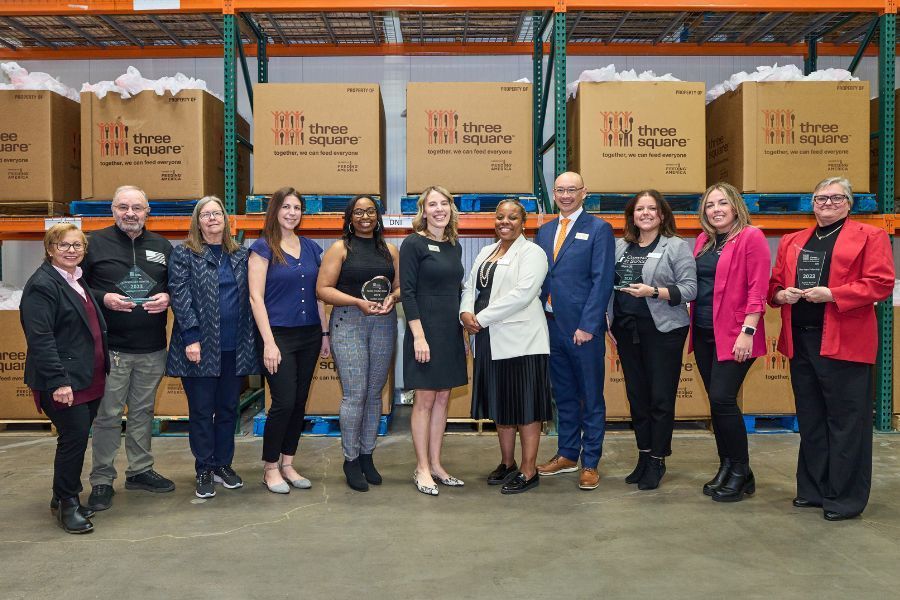 Group of people in a warehouse, posing with awards in front of boxes