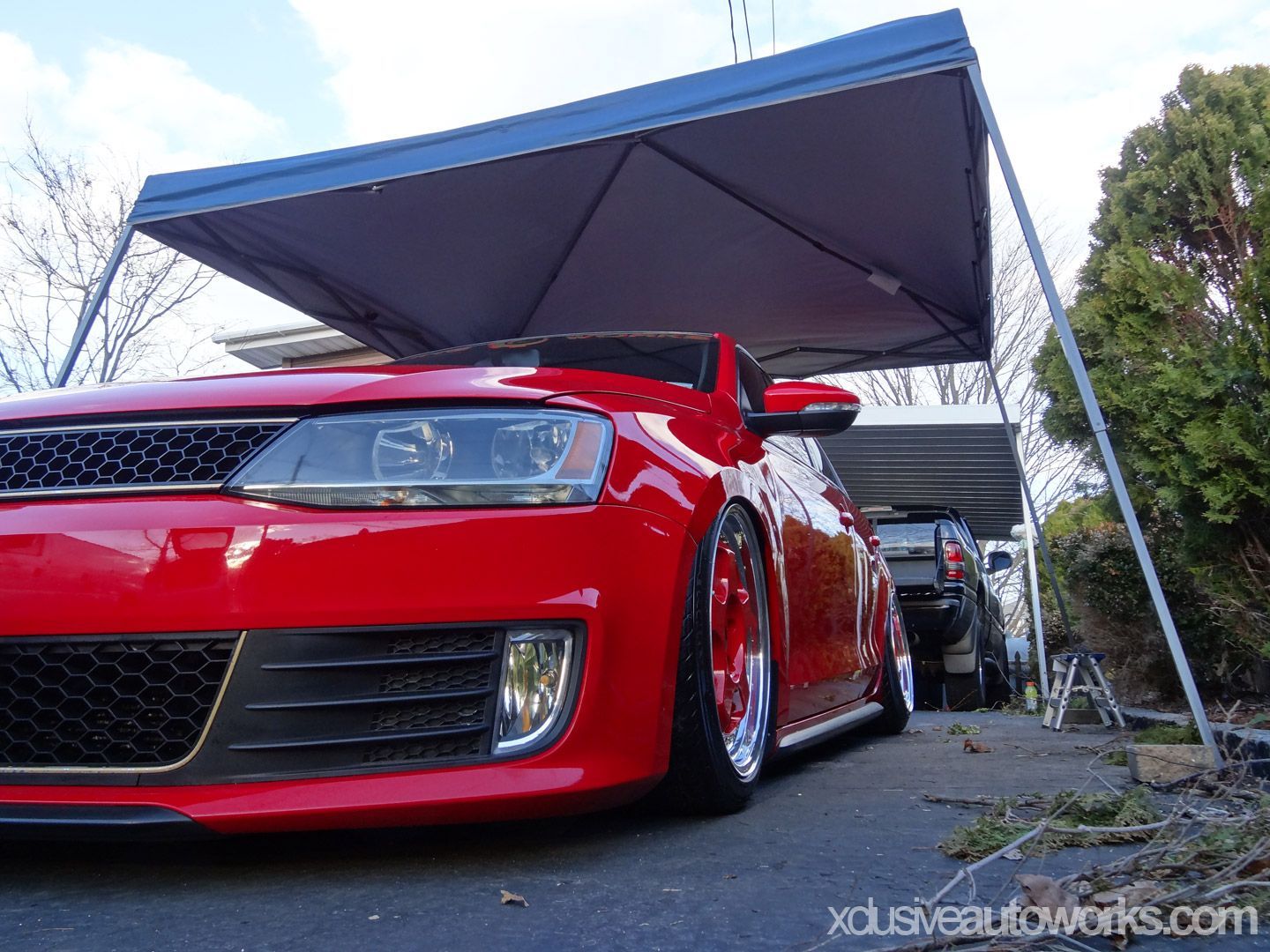 A red car is parked under a canopy in a driveway.