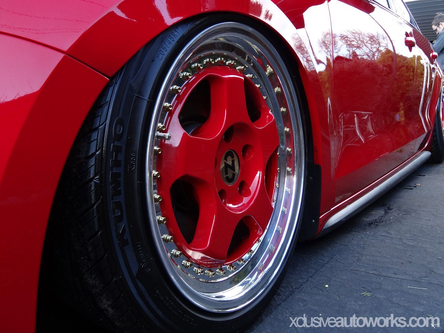 A close up of a red car wheel with xclusiveautoworks.com written on the bottom