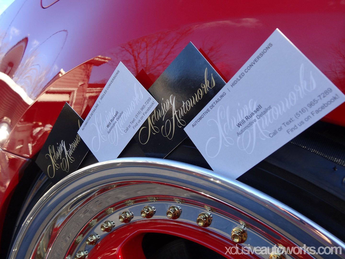 Three business cards are stacked on top of a red car wheel