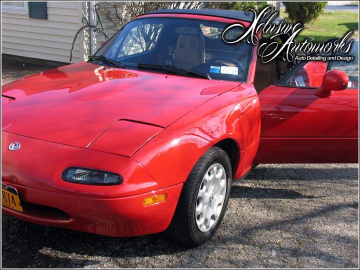 A red sports car is parked in a driveway with the door open