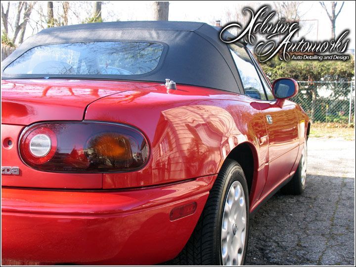 A red sports car with a black top is parked in a parking lot