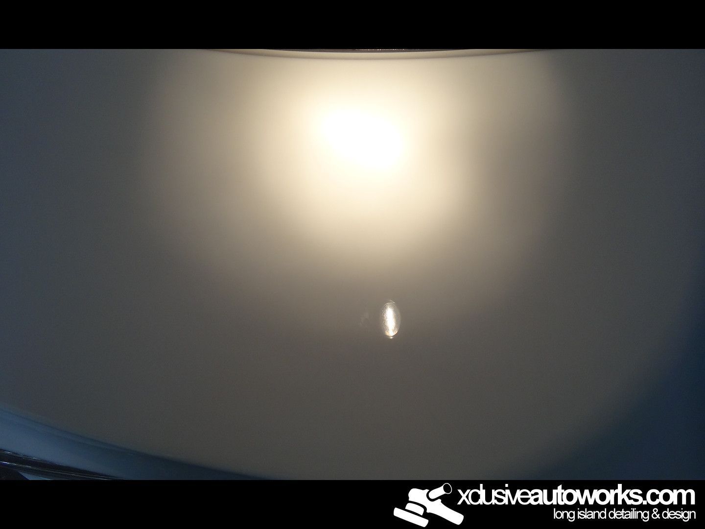 A light is shining on a white surface with xclusiveautoworks.com written on the bottom