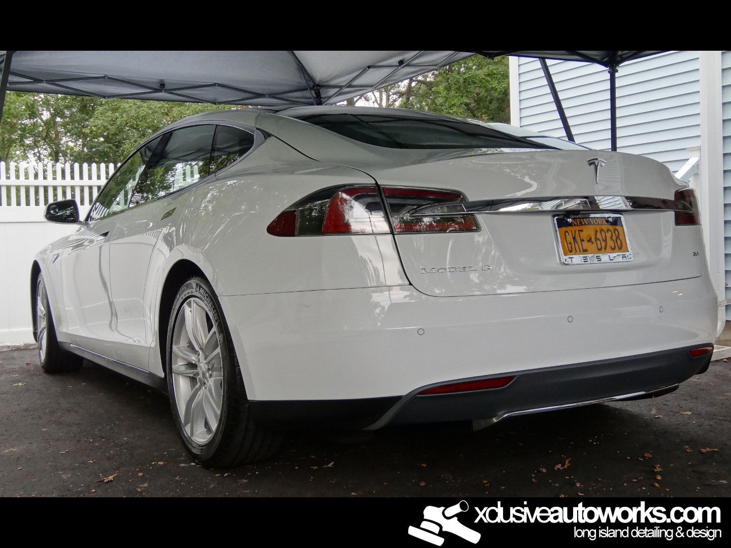 A white tesla model s is parked under a tent.