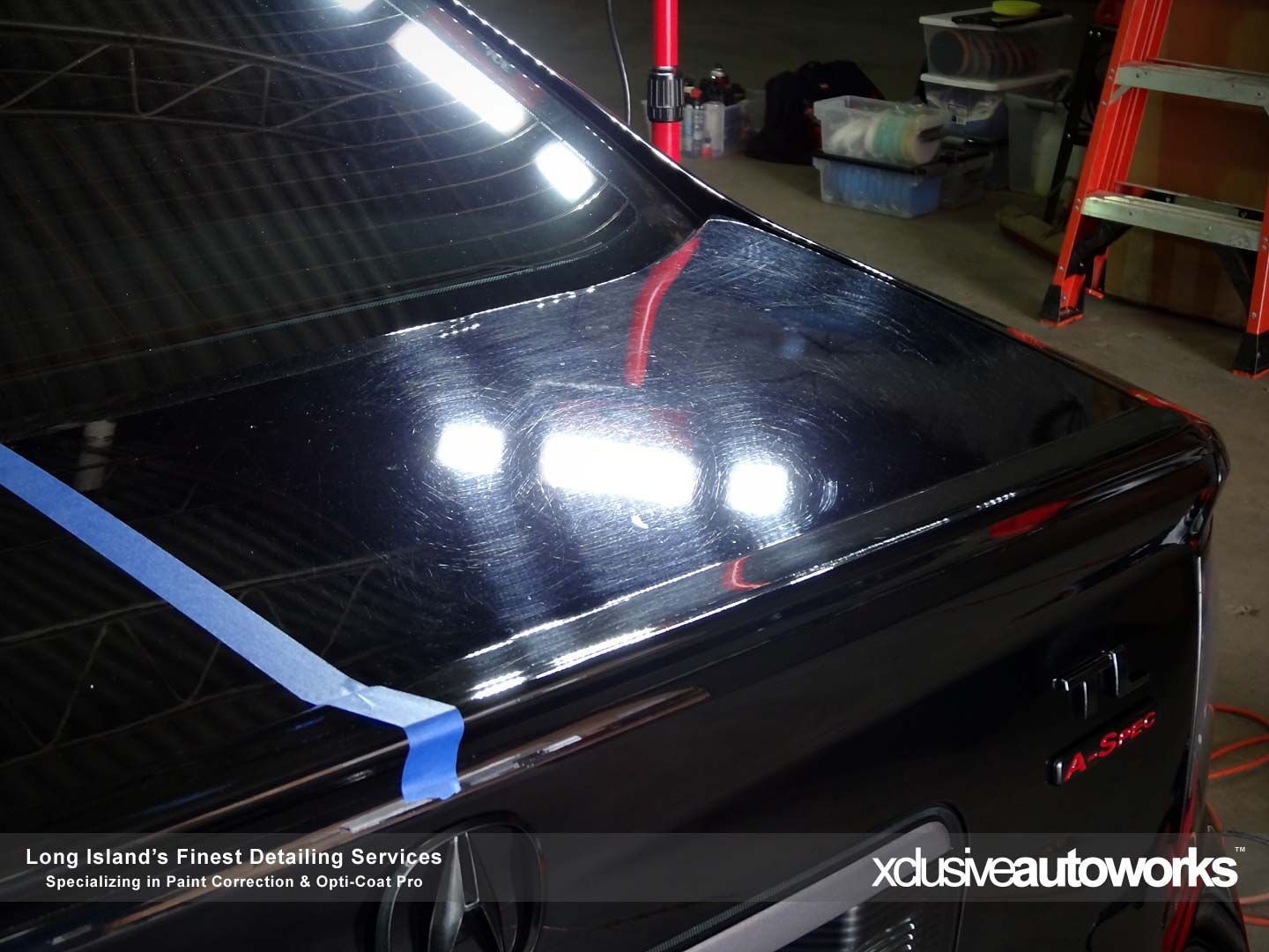 A black car with a blue tape on the hood is sitting in a garage.