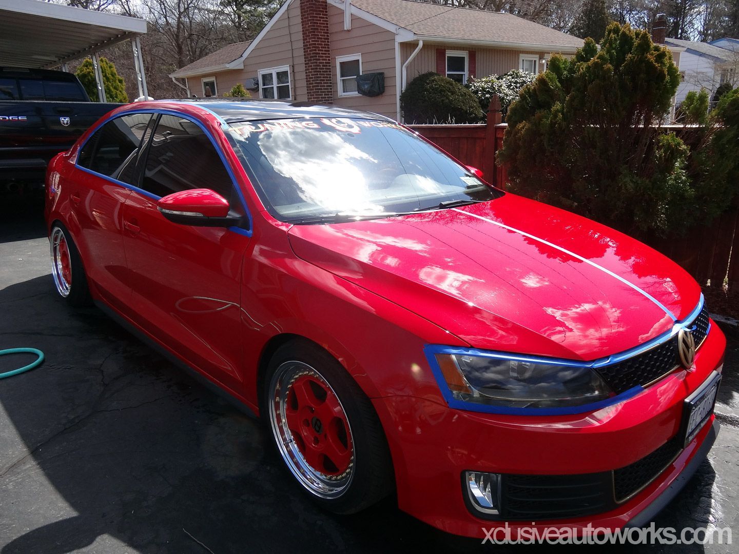 A red car with blue trim is parked in front of a house