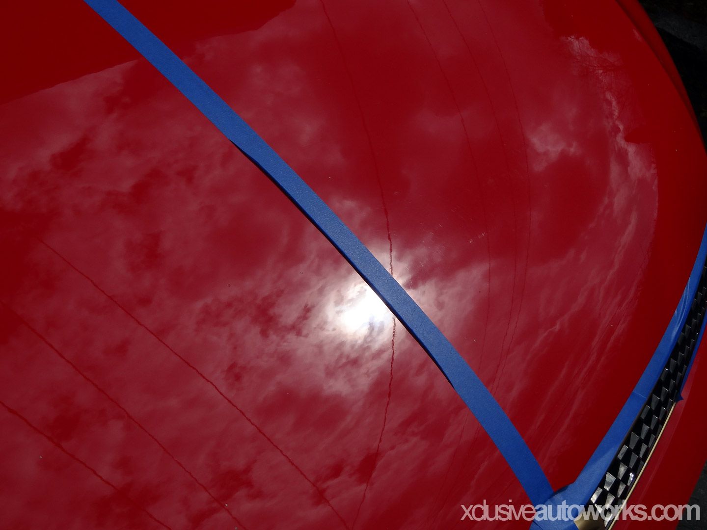 A close up of a red car with xclusiveautoworks.com written on the bottom