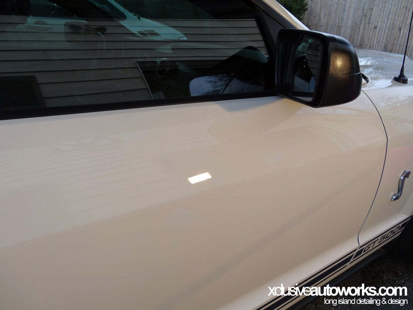 A white car is parked in front of a wooden house.