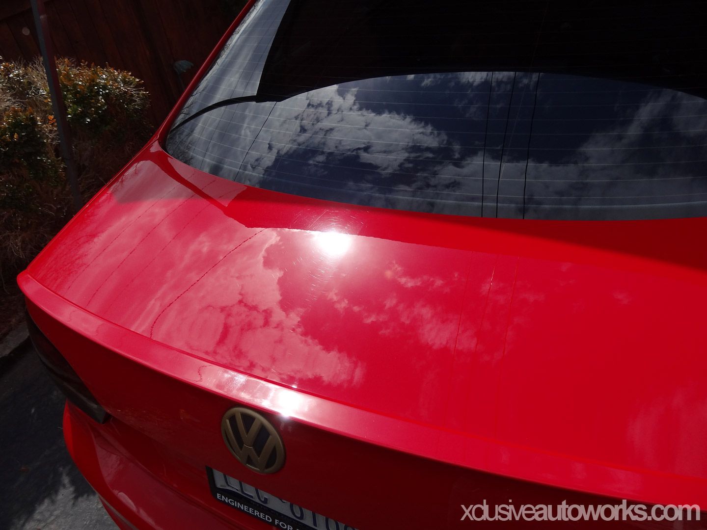 A red vw car is parked in front of a wooden fence
