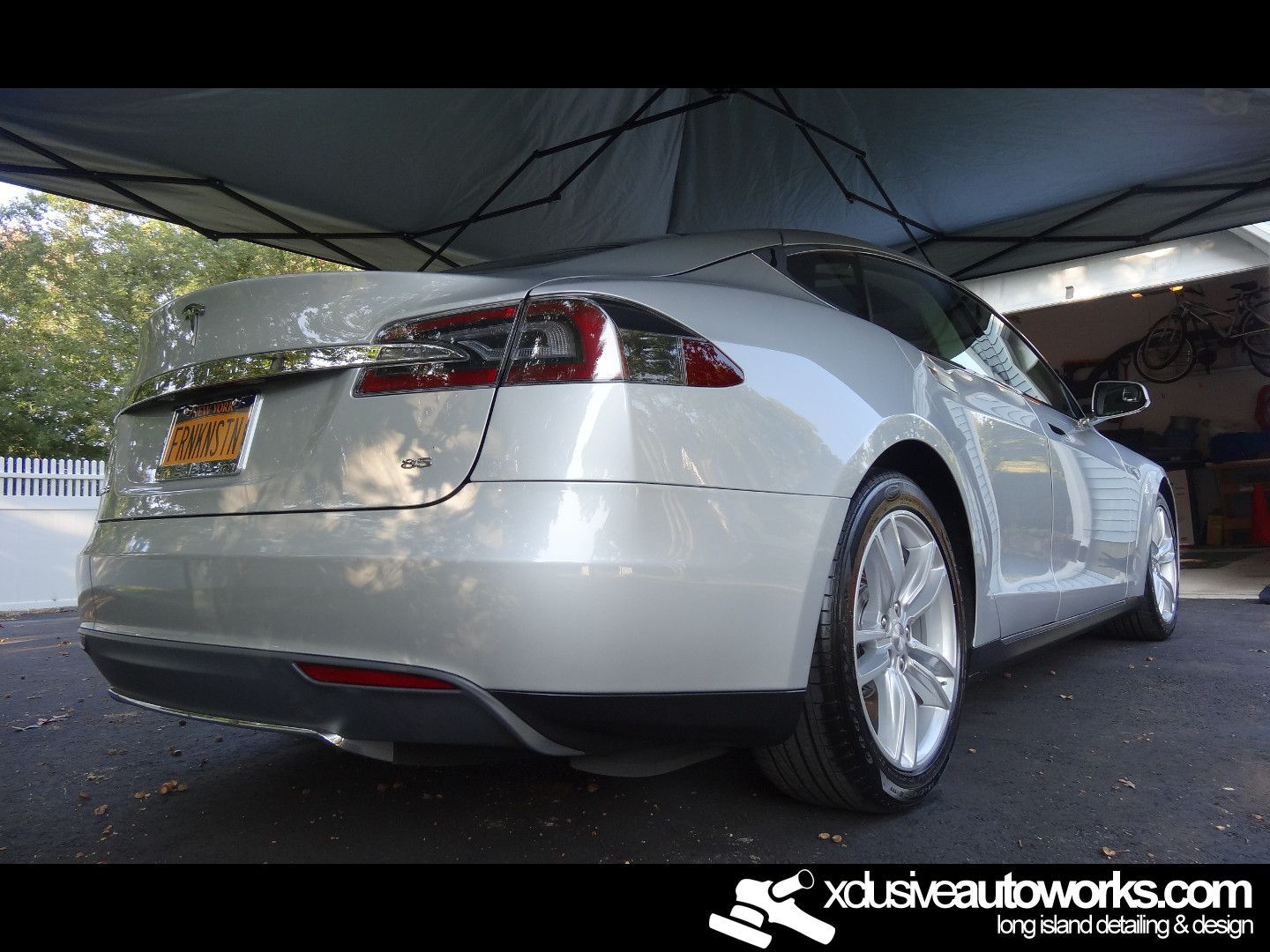 A silver tesla model s is parked under a tent