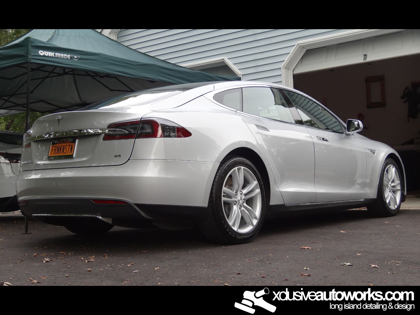 A silver tesla model s is parked in front of a garage.