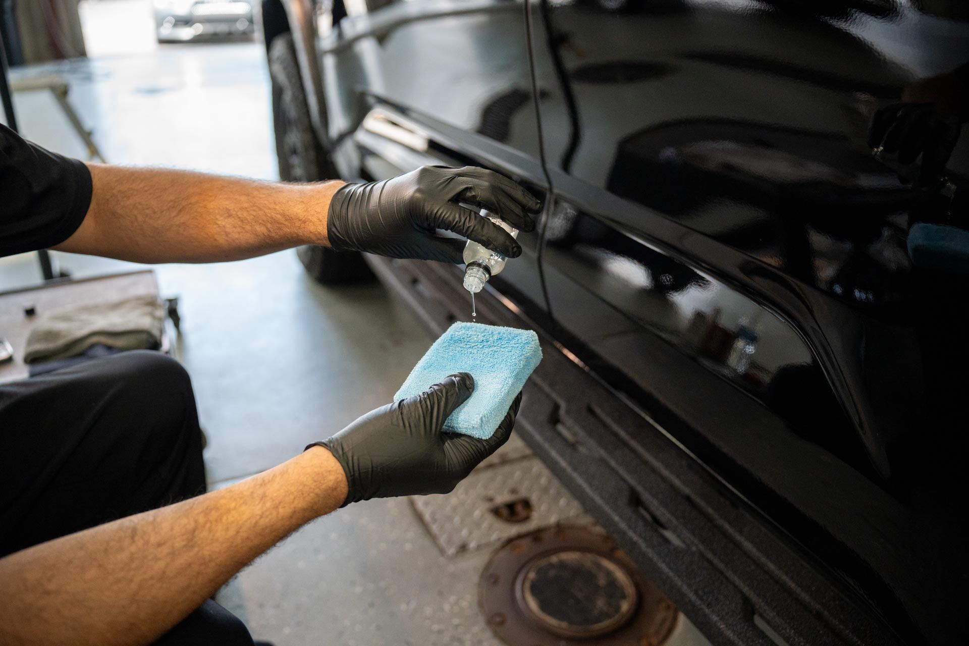 A man is cleaning the hood of a black car with a cloth.