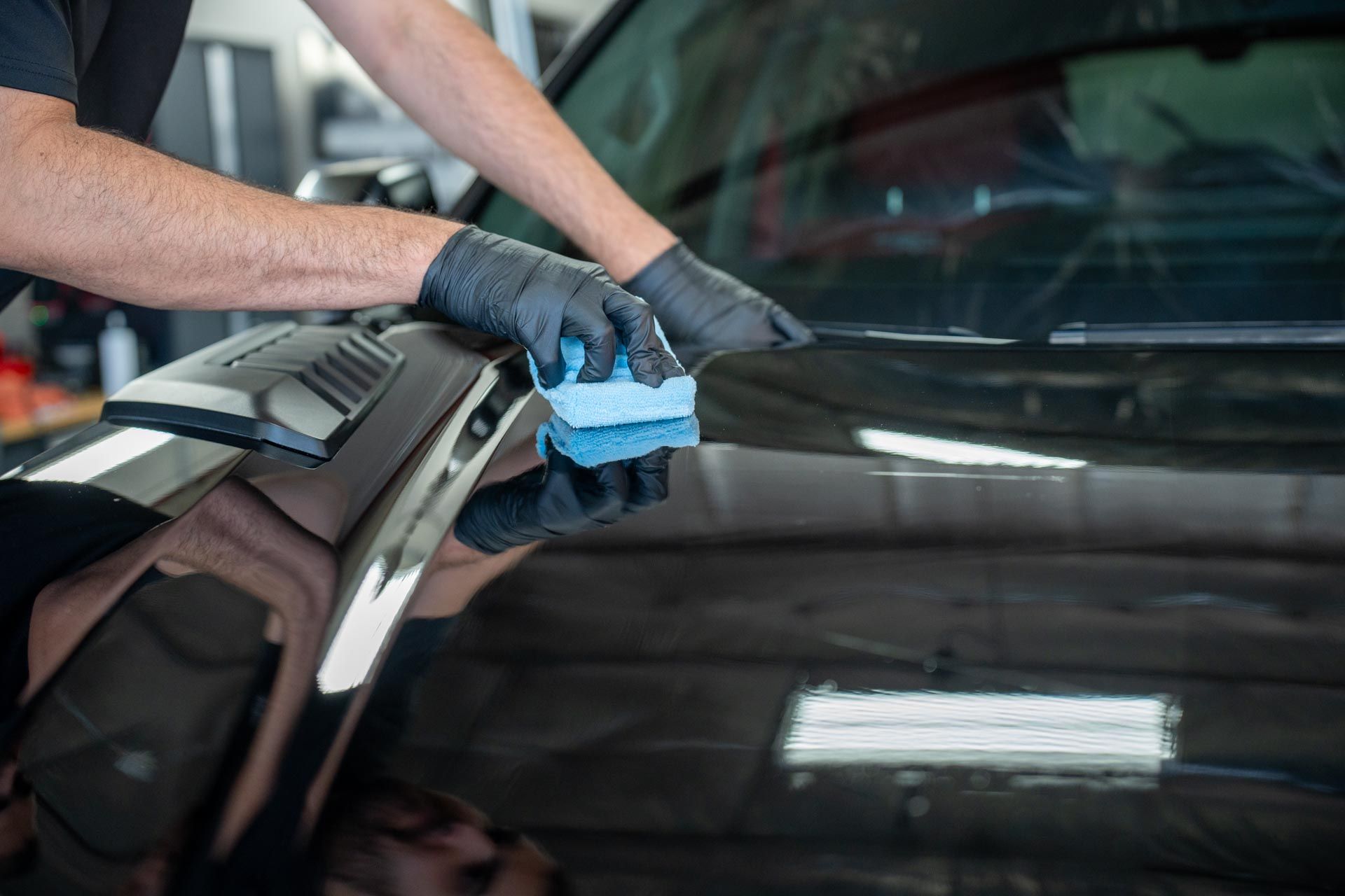 A man is cleaning the hood of a black car with a cloth.