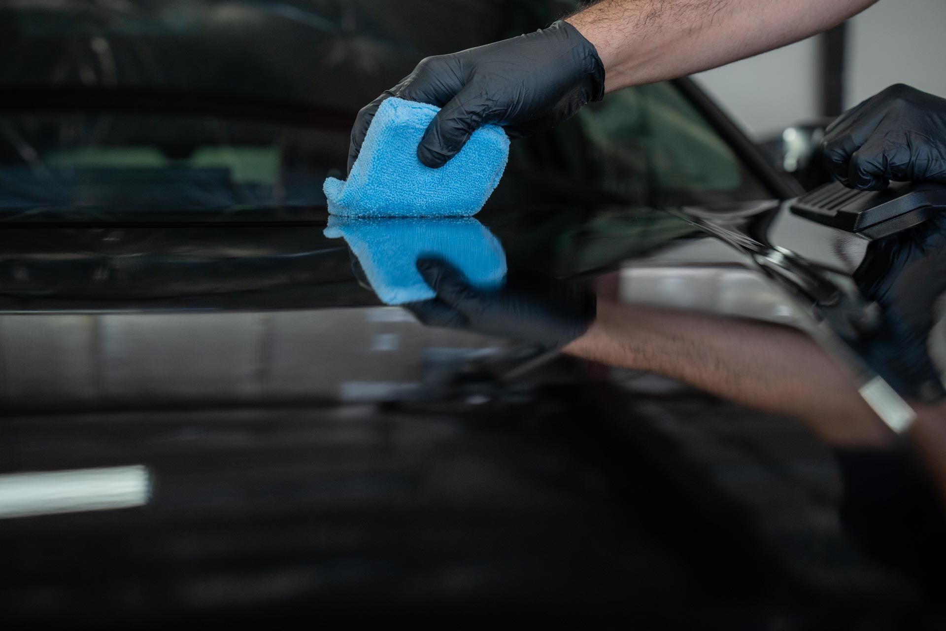 A man is cleaning the hood of a black car with a cloth.