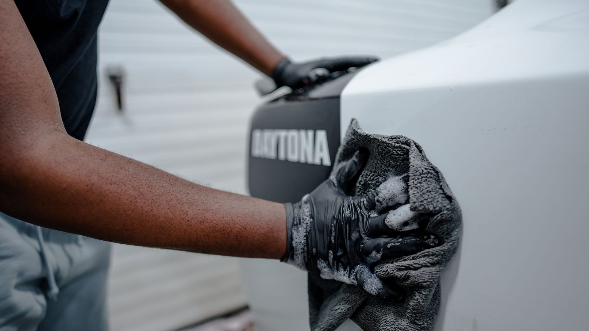 A man is cleaning a car with a towel and gloves.