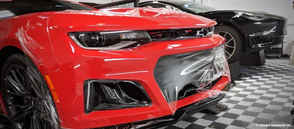 A red car is parked next to a black car in a garage.