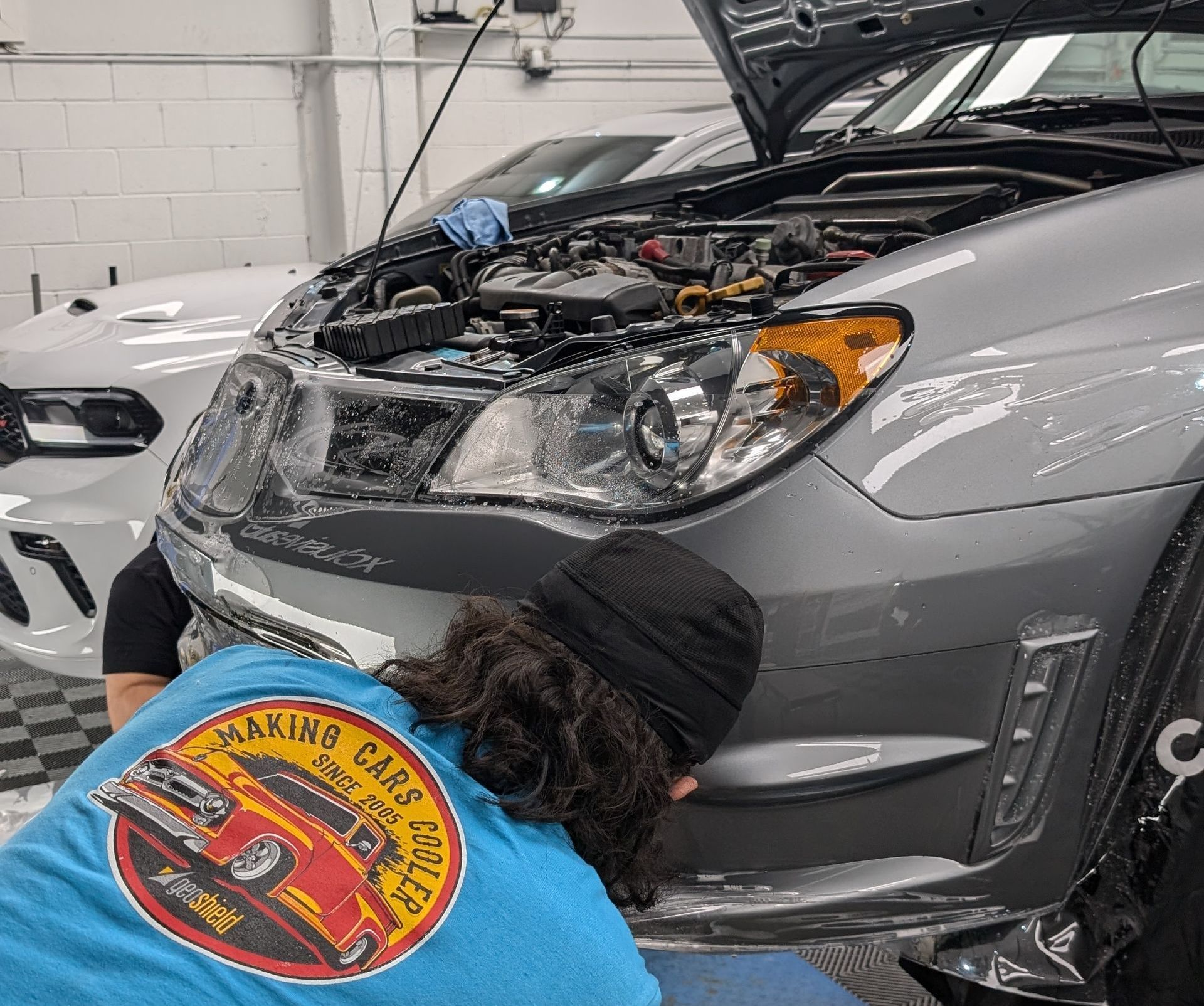 A man in a blue shirt is working on the front of a car.