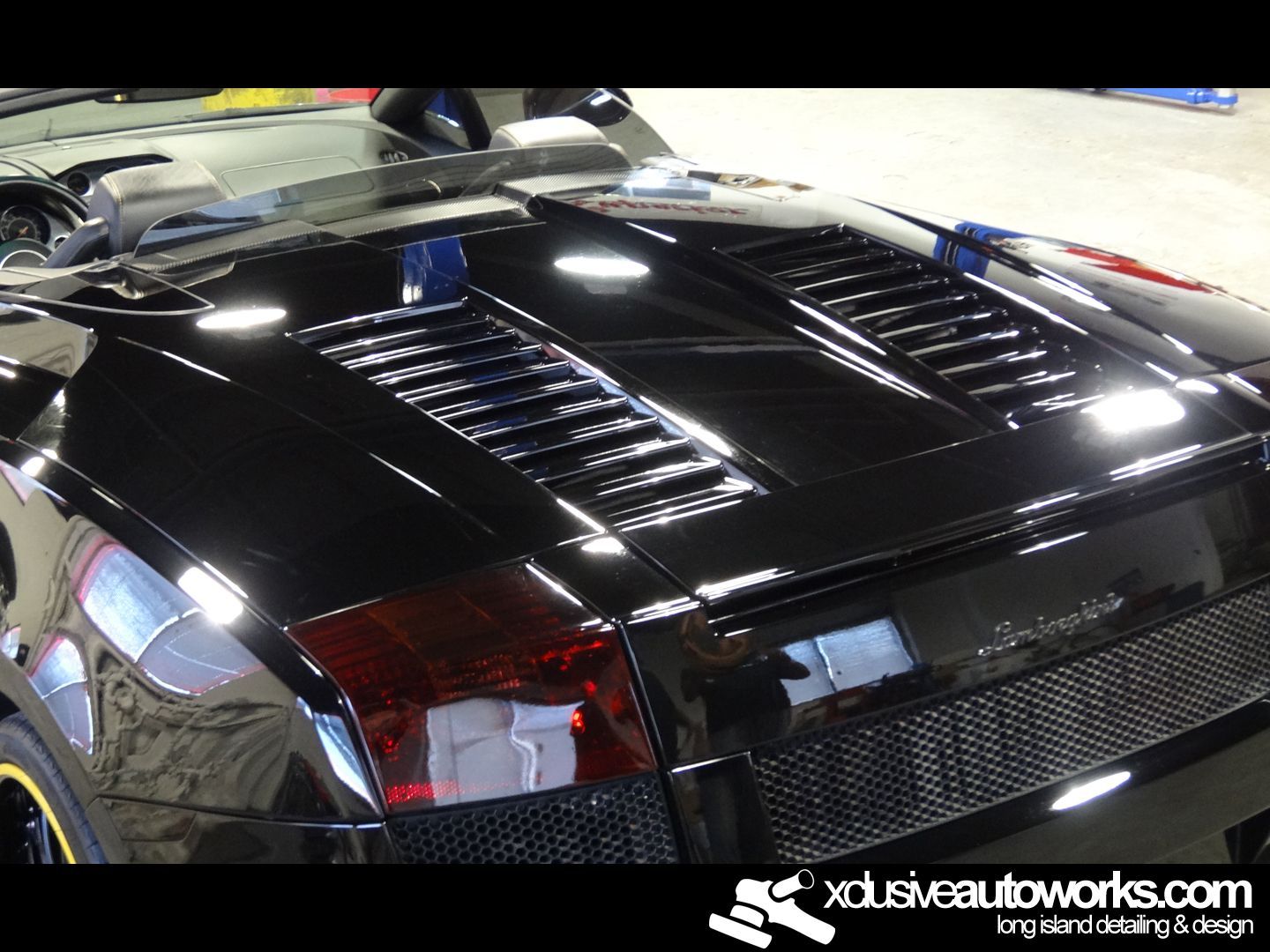 A black lamborghini is sitting in a garage with xdusveautoworks.com written on the bottom
