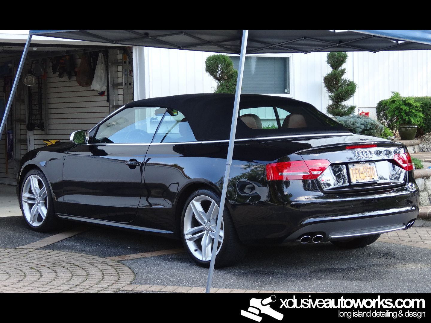 A black audi a5 convertible is parked under a canopy in a garage.