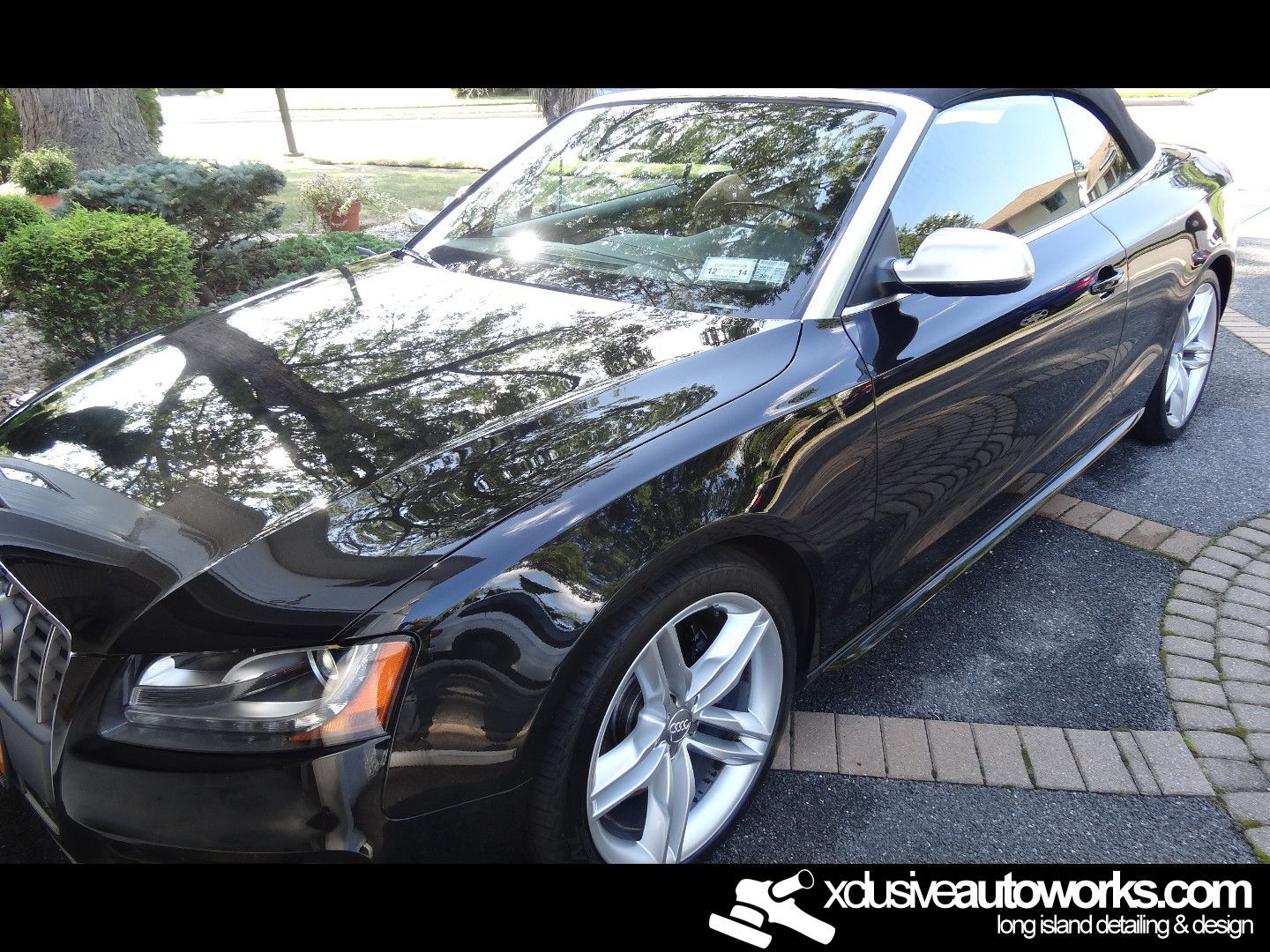 A black convertible car is parked in a driveway.