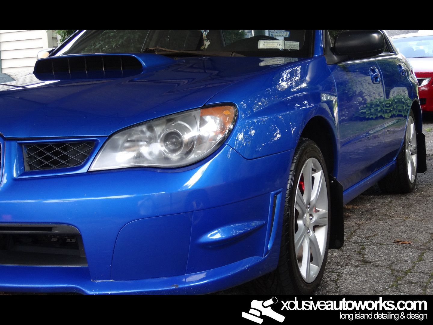 A blue car is parked in front of a xdusveautoworks.com sign