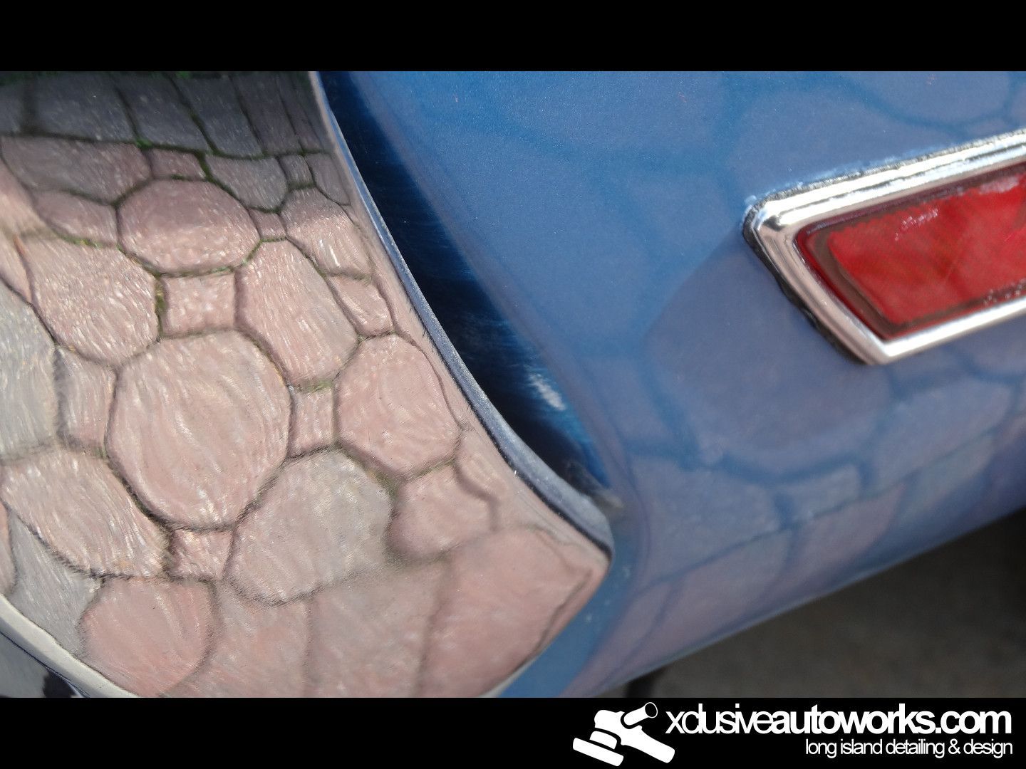 A blue car is parked next to a brick walkway with xdusveautoworks.com written on the bottom