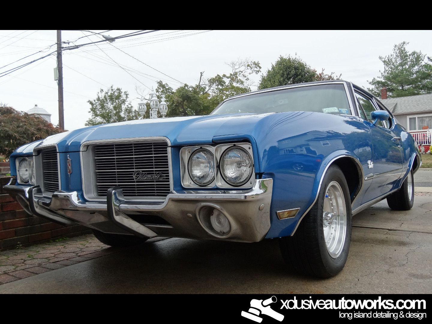 A blue oldsmobile cutlass supreme is parked in front of a house.
