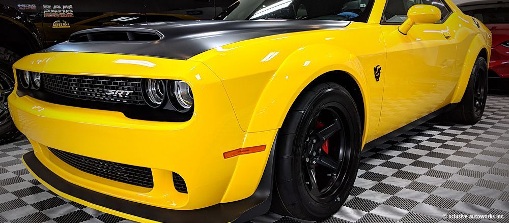 A yellow dodge challenger demon is parked in a garage.