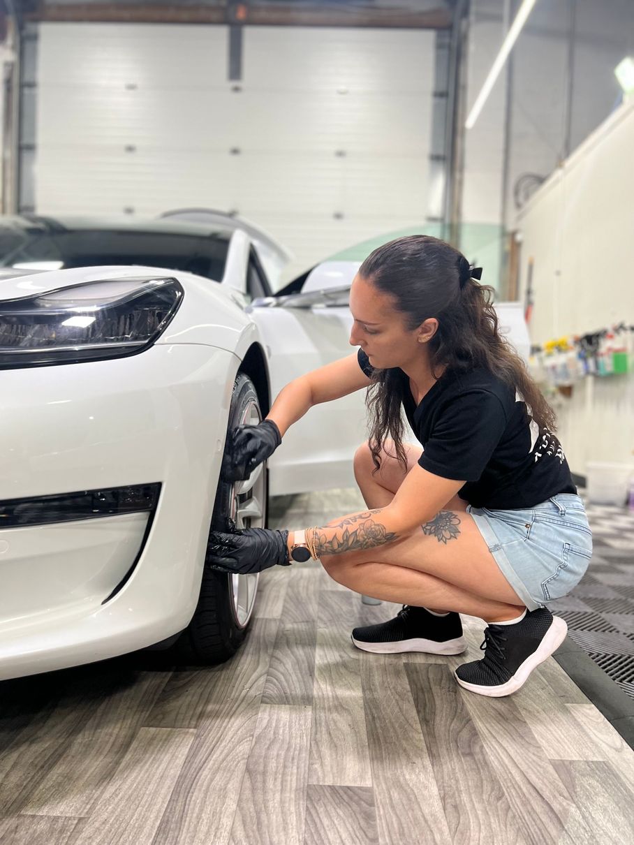 A woman is kneeling down next to a white car.