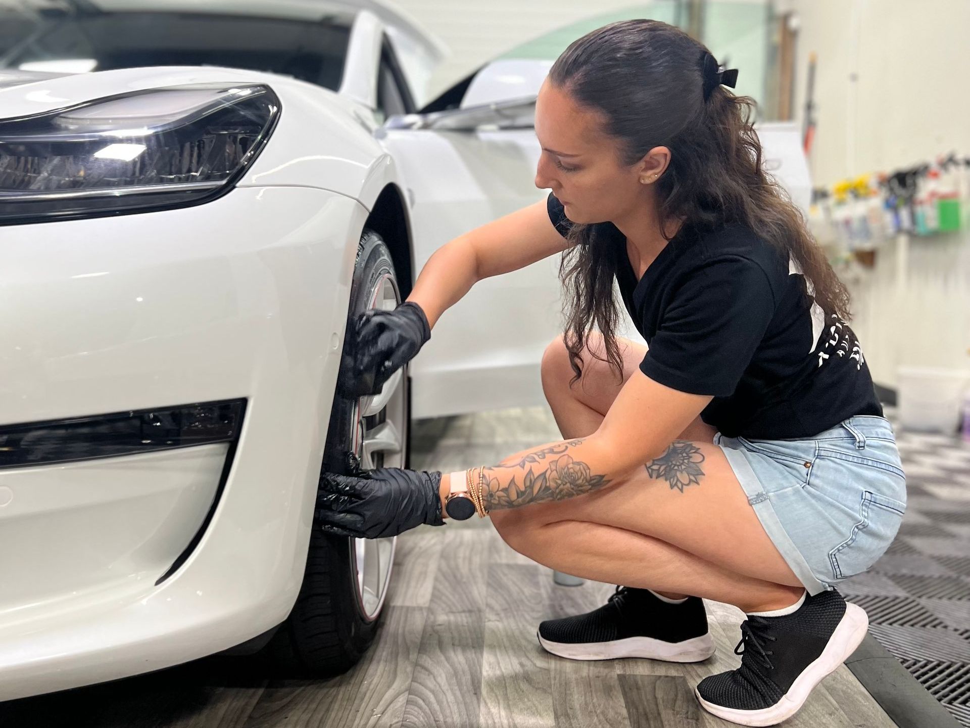 A woman is kneeling down next to a white car.