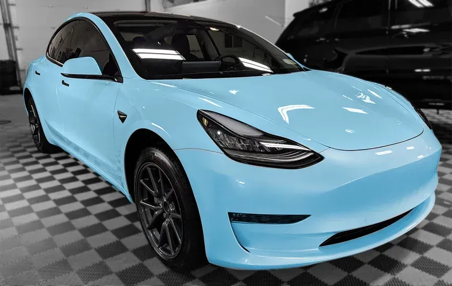 A light blue tesla model 3 is parked in a garage.