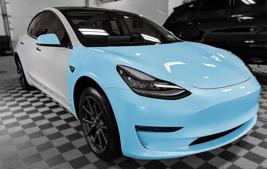 A tesla model 3 is sitting on a checkered floor in a garage.