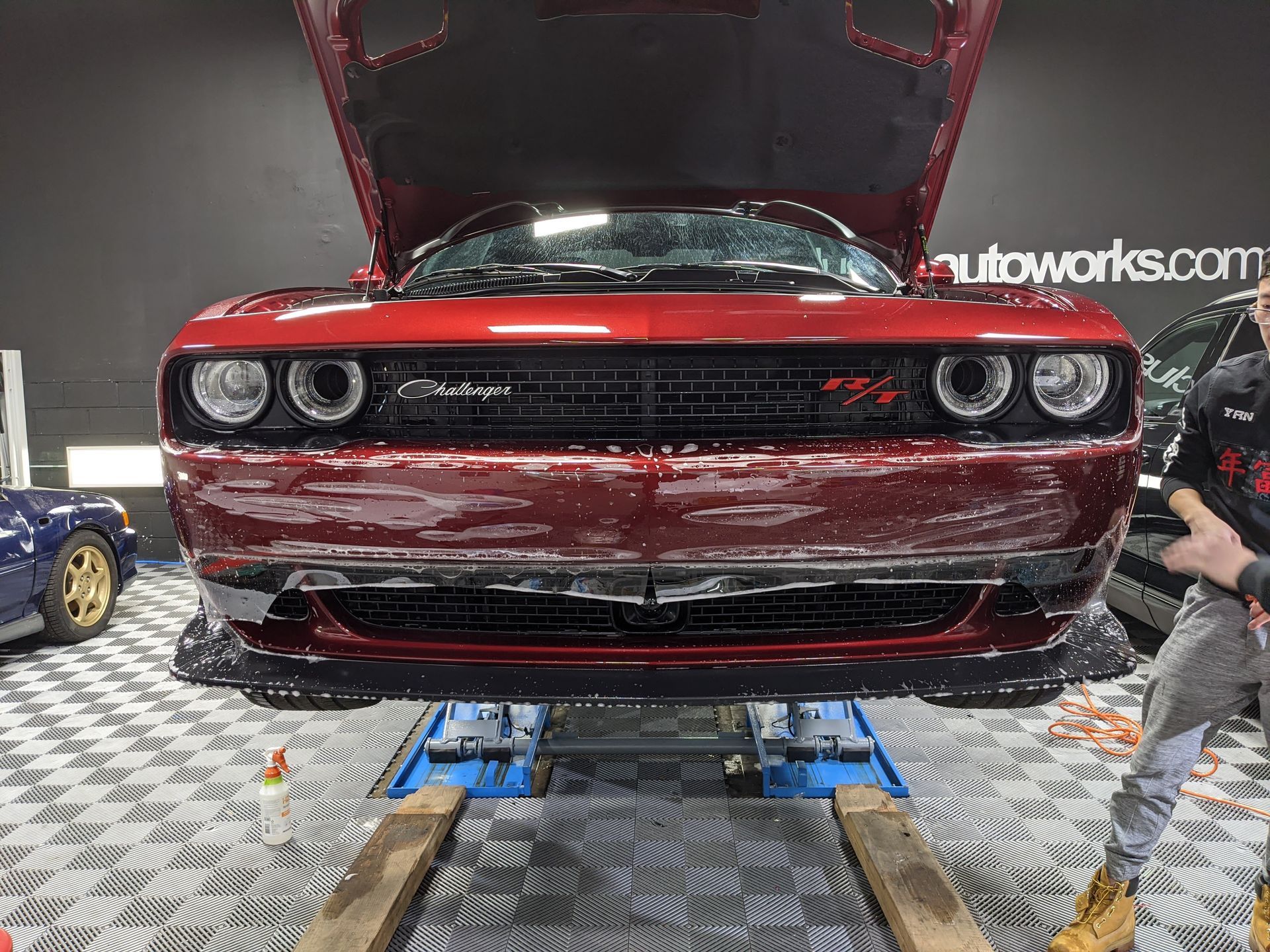 A man is standing in front of a red dodge challenger with the hood up.