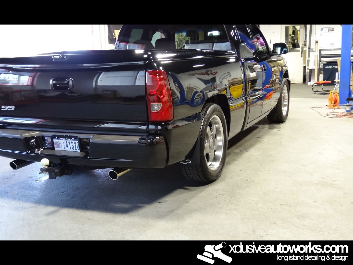 A black truck is parked in a garage with xdusveautoworks.com written on the bottom