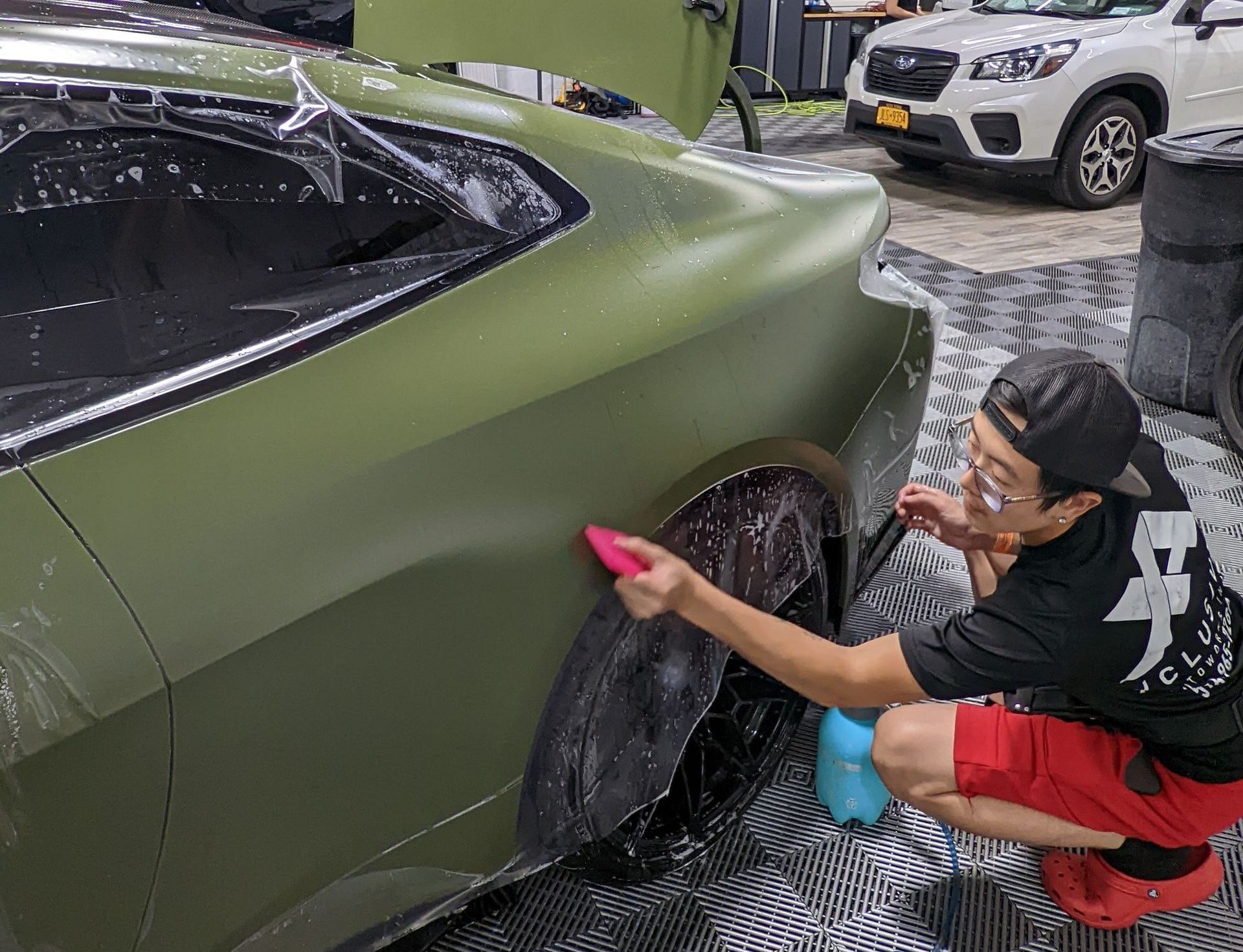 A man is kneeling down next to a green car.