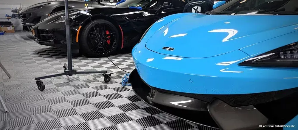 A blue sports car is parked next to a black sports car in a garage.