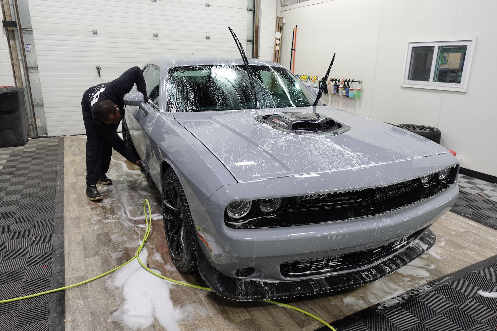 A man is washing a gray dodge challenger in a garage.