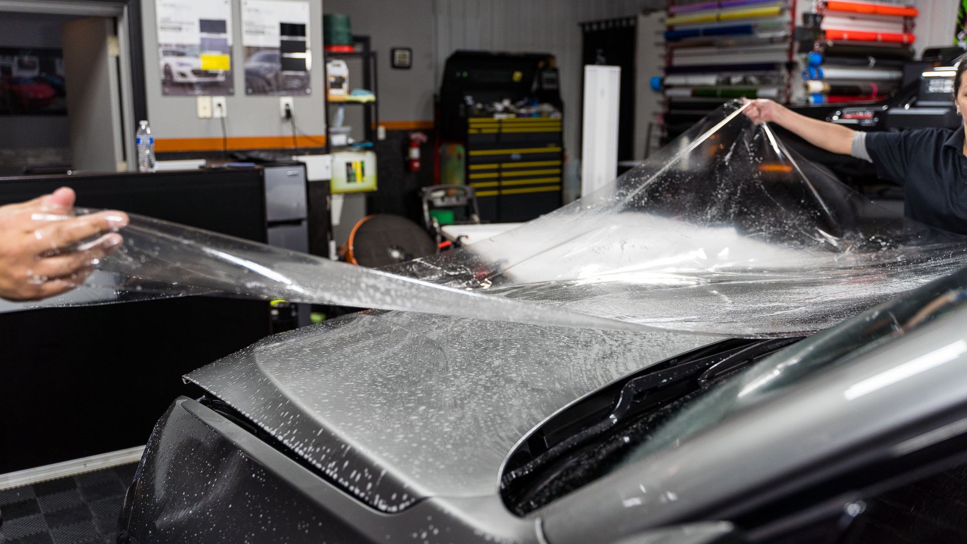 A man is cleaning the hood of a black car with a cloth.