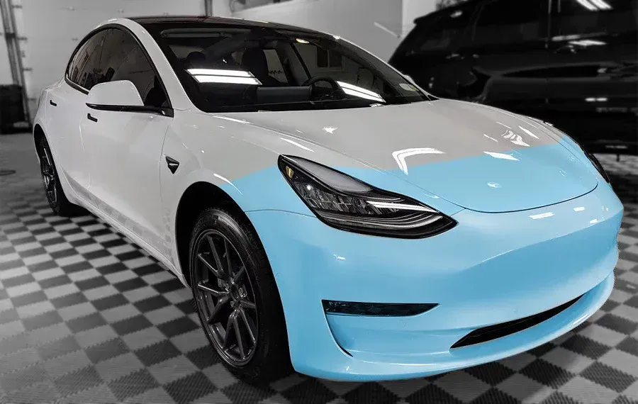 A white tesla model 3 is sitting on a checkered floor in a garage.