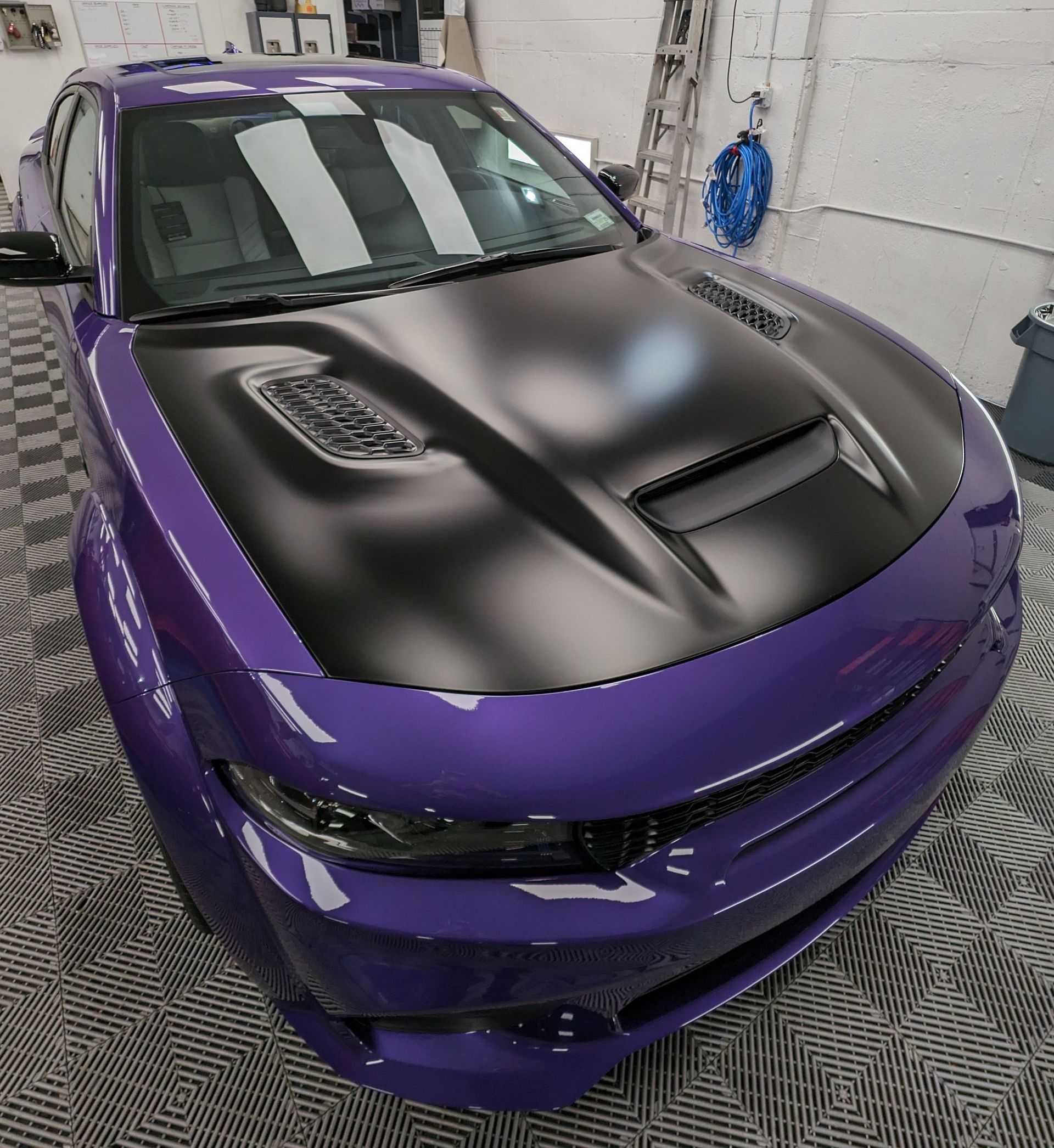 A purple car with a black hood is parked in a garage