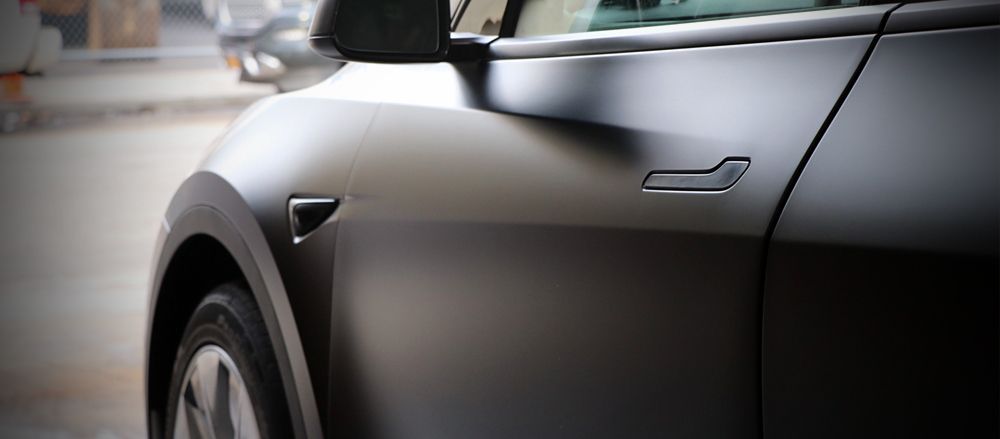 A close up of the side of a black tesla model 3.