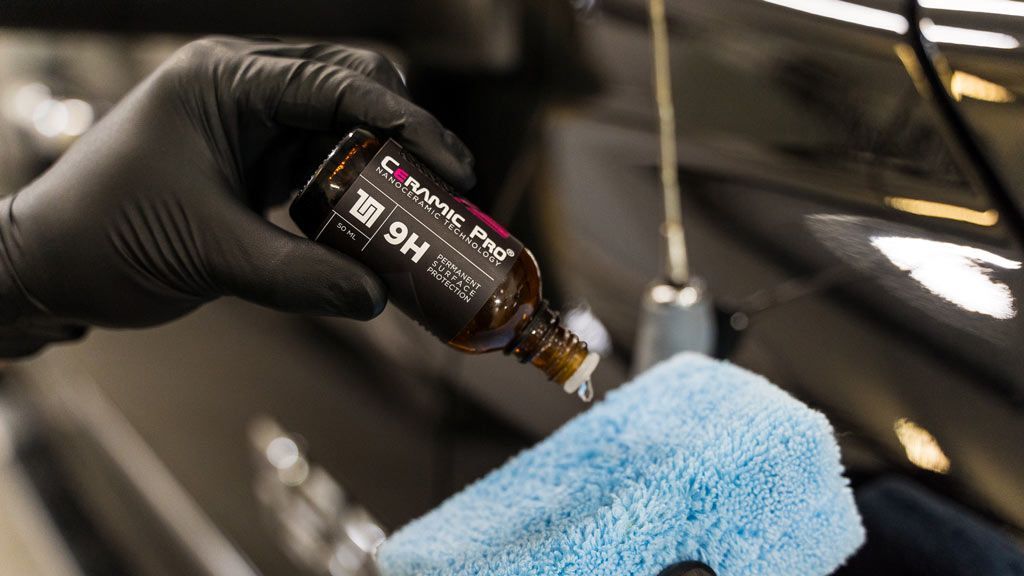 A man is cleaning the hood of a black car with a cloth.