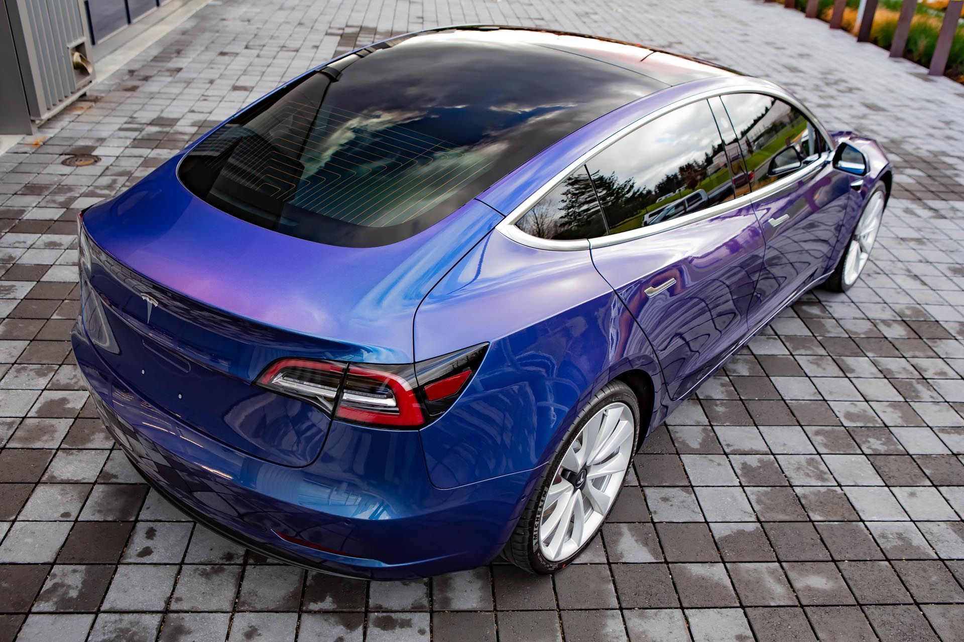 A blue tesla model 3 is parked on a brick driveway.