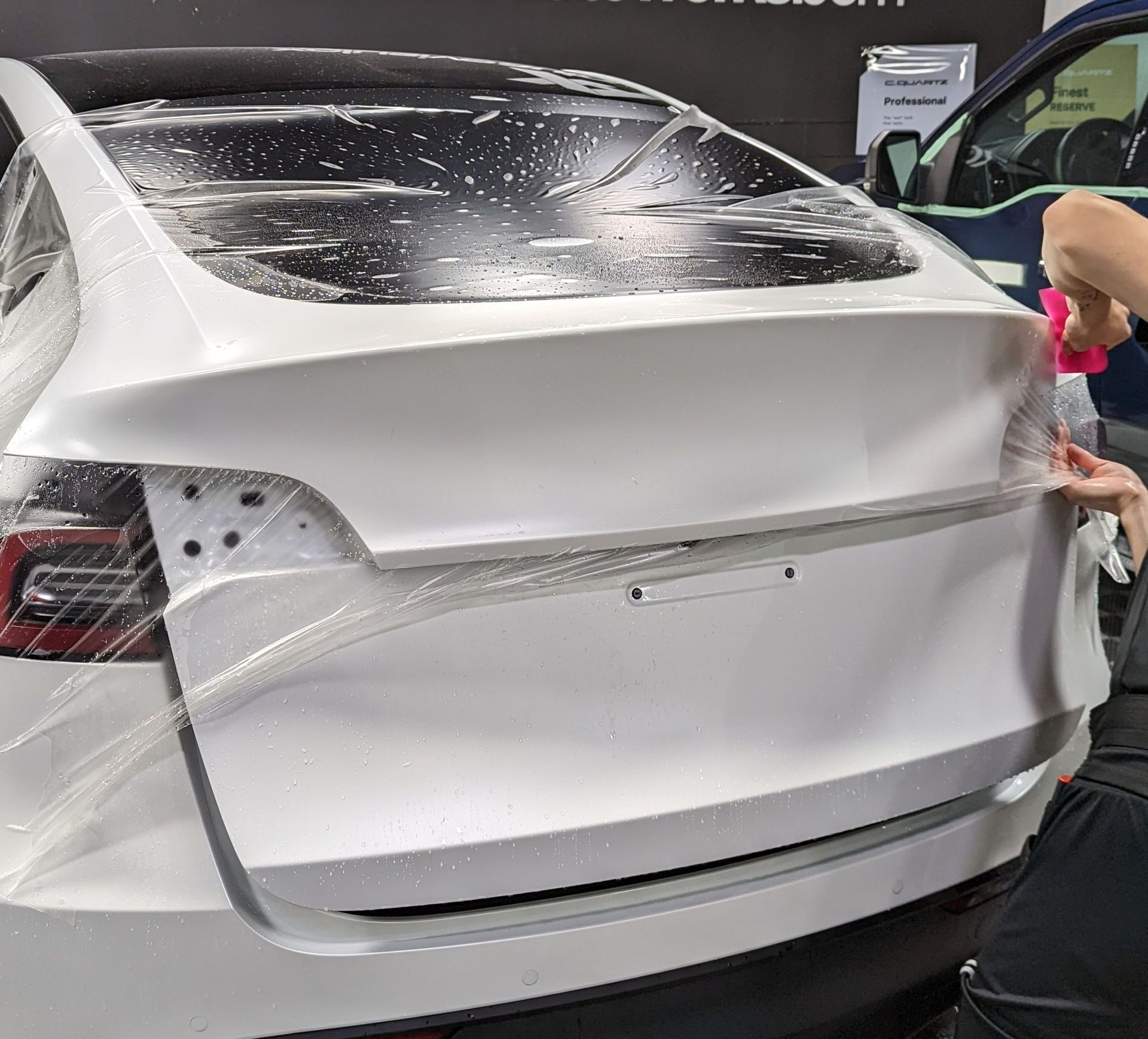 A person is wrapping a white car with plastic wrap.