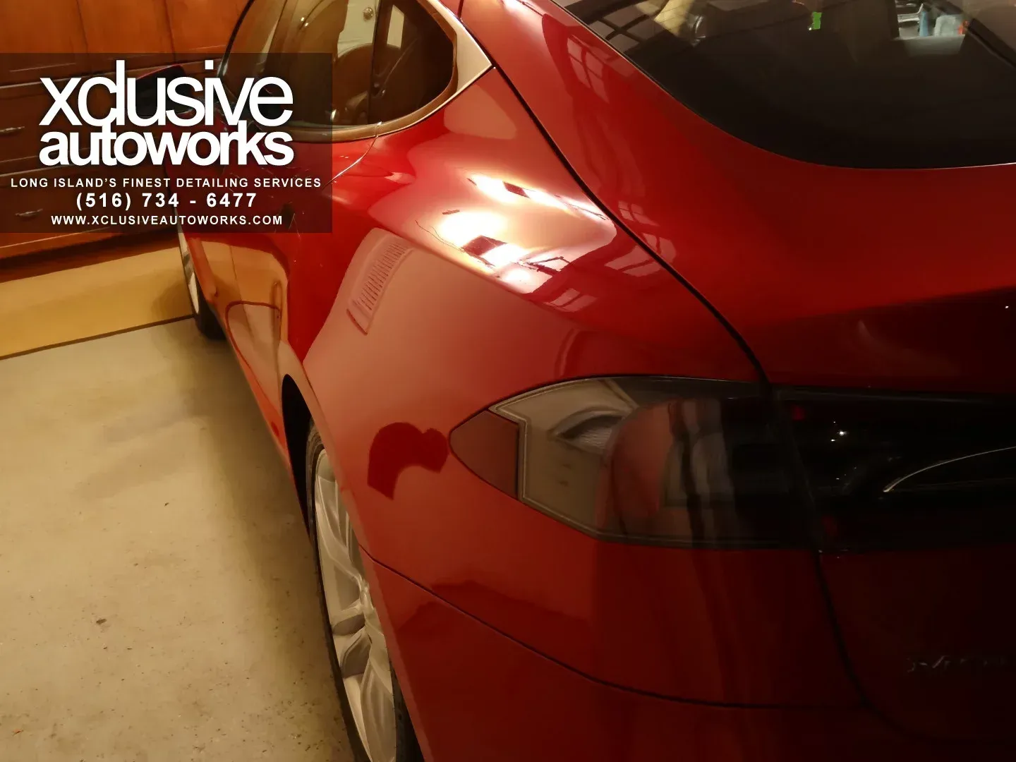A red car from xclusive autoworks is parked in a garage